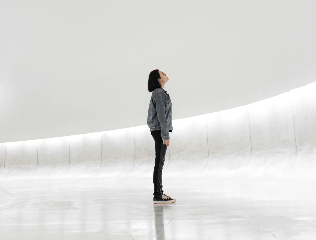 Person steht in einer großen, hellen, minimalistischen Architektur und blickt nach oben.