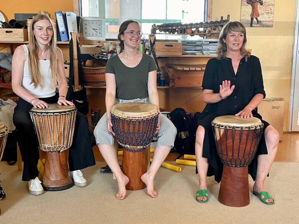 Q-Crew beim Trommelkurs im Mannheimer Trommelpalast: Drei Teilnehmende sitzen an Djembe-Trommeln und üben gemeinsam Rhythmen – Sommerevent und Teambuilding.