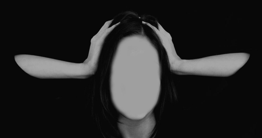 Schwarzweißes Symbolbild: Person hält den Kopf mit beiden Händen, Gesicht anonymisiert – Visualisierung von Belastung und Trauma im Kontext sexualisierter Gewalt und Vergewaltigung.