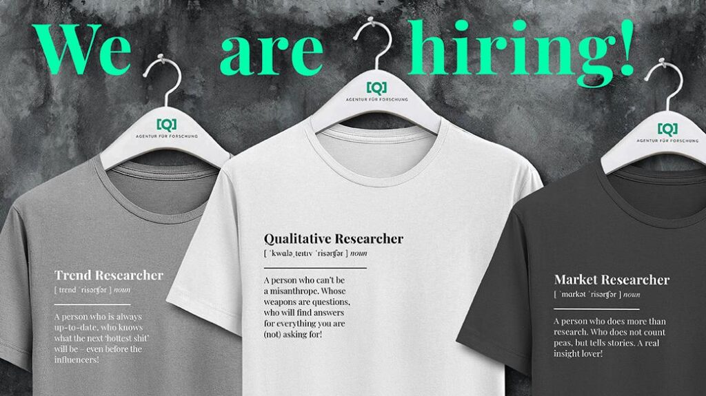 Banner „We are hiring!“ mit drei Q-T-Shirts auf Bügeln („Trend Researcher“, „Qualitative Researcher“, „Market Researcher“) – Recruiting-Motiv für Jobs in qualitativer Marktforschung bei Team Q.