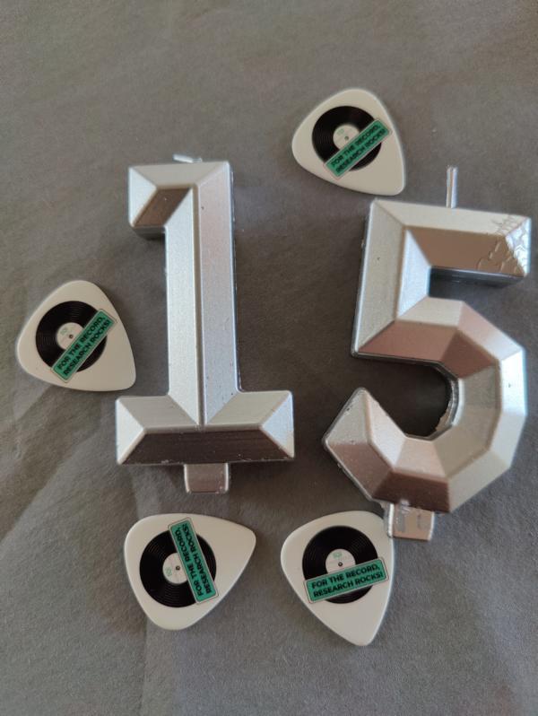 Dekoration zur Q15 Jubiläumsparty: silberne Zahlen „15“ mit Gitarren-Plektren im Vinyl-Design und Schriftzug „For the Record, Research Rocks“.