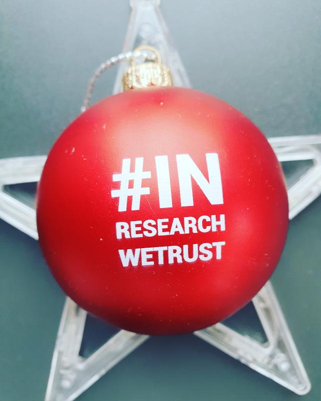 Rote Weihnachtskugel mit Aufdruck „#IN RESEARCH WE TRUST“ auf Stern-Deko – Symbolbild für Q Weihnachtsaktion, Teamkultur und Marktforschung in der Adventszeit.