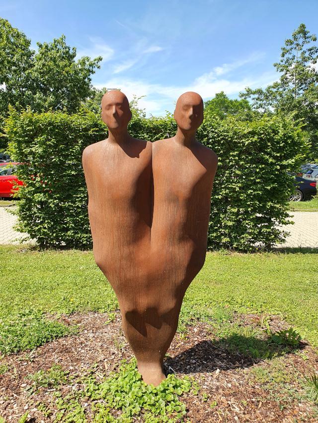 Moderne Outdoor-Skulptur aus rostfarbenem Metall mit zwei gesichtslosen Figuren, die zu einem Körper verschmelzen – Symbolbild für Netzwerk- und Datenanalyse sowie Q News rund um Data Science und KI.